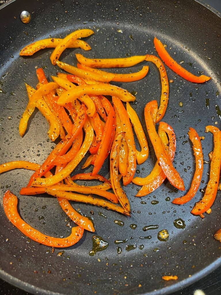 Slightly browned, sautéed, sliced orange and red bell peppers in a non-stick pan.