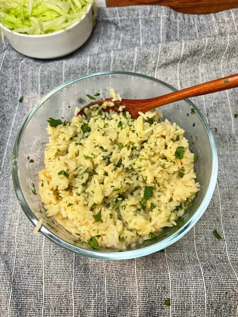 A glass bowl of cilantro lime rice with a long wooden spoon in the bowl.