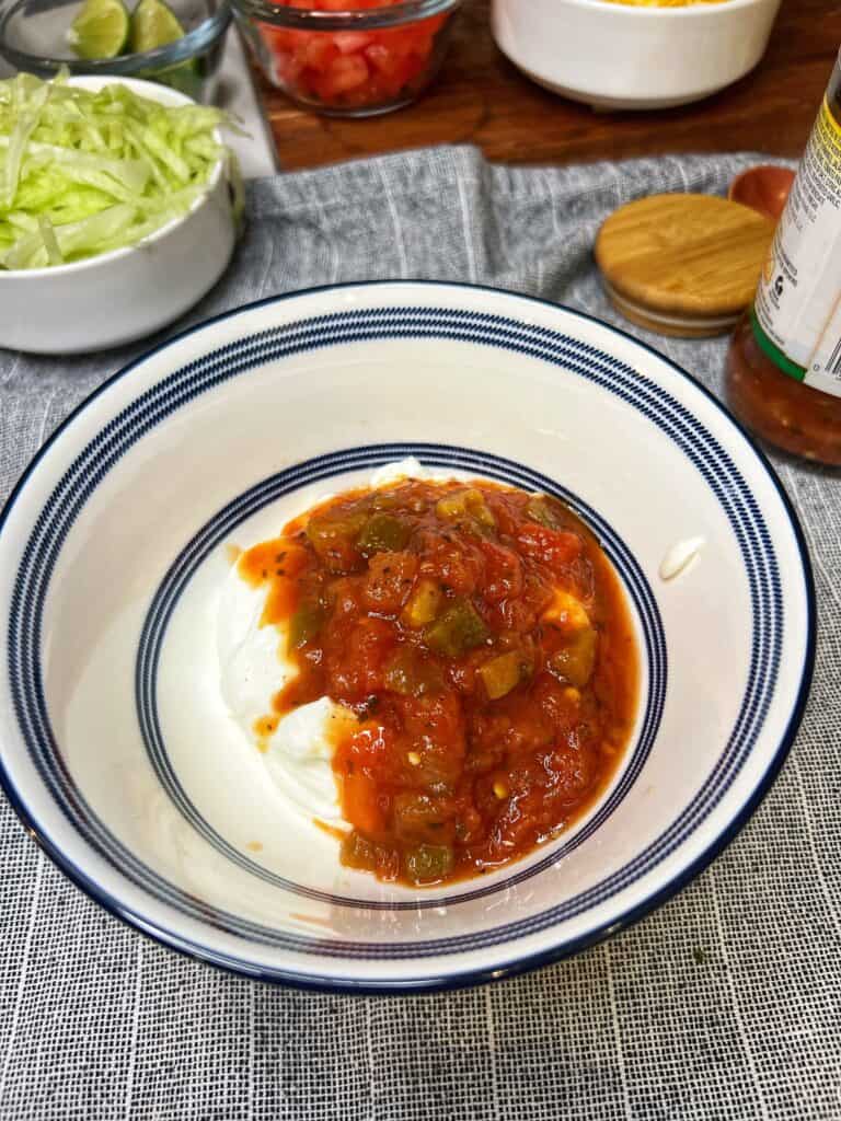 A white bowl trimmed in blue holding sour cream and salsa.