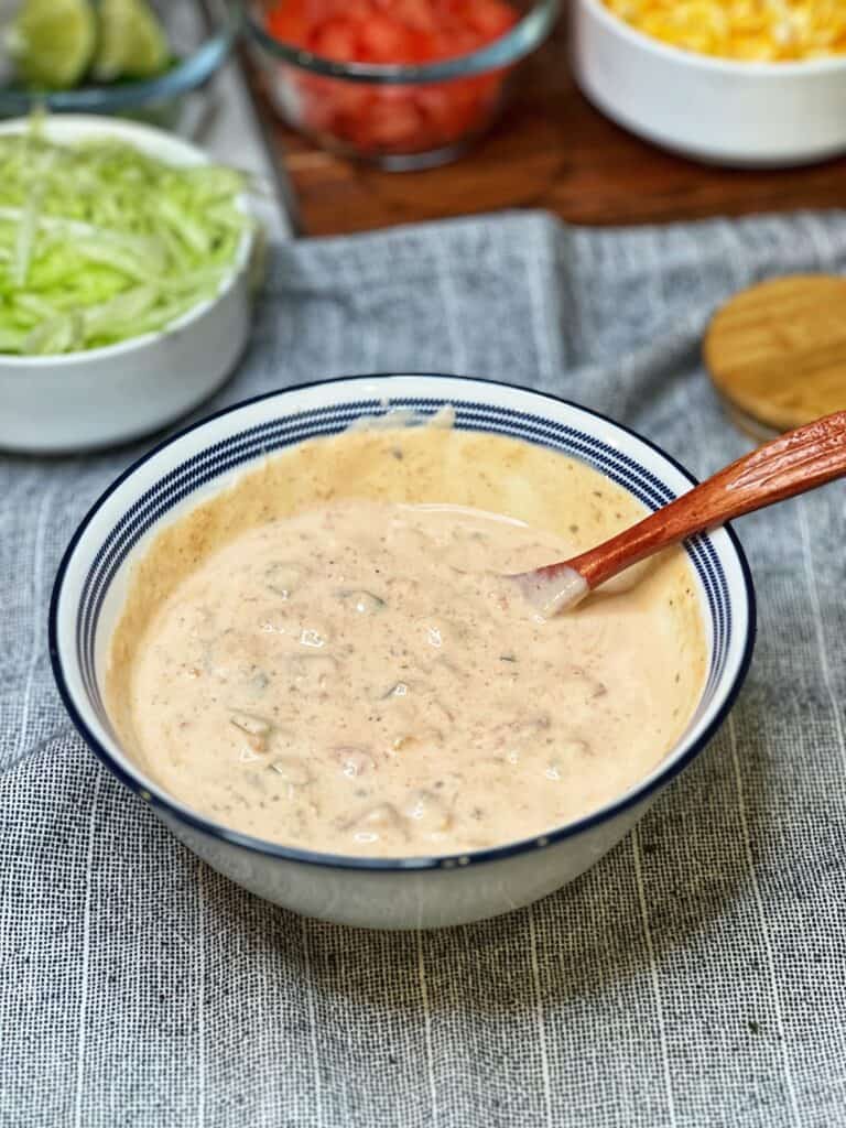 A white bowl trimmed in blue of taco dressing with a long wooden spoon in the bowl.