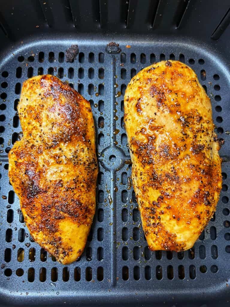 Two air fried chicken breasts sitting in an air fryer basket.