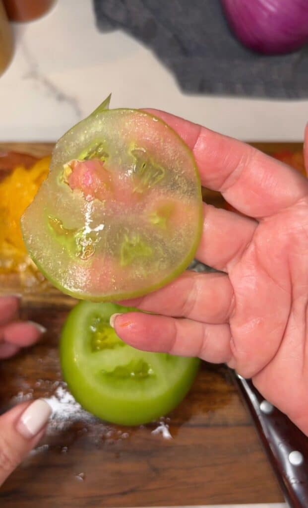 Me holding a paper thin slice of a green heirloom tomato.