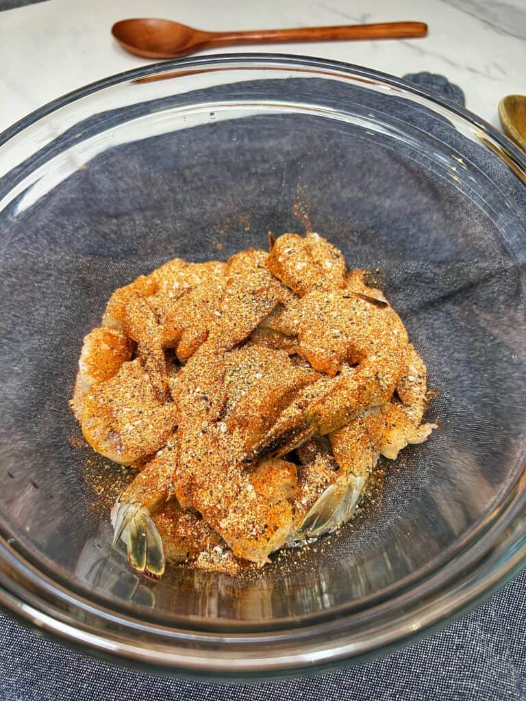 A glass bowl of raw shrimp sprinkled with olive oil and spices.