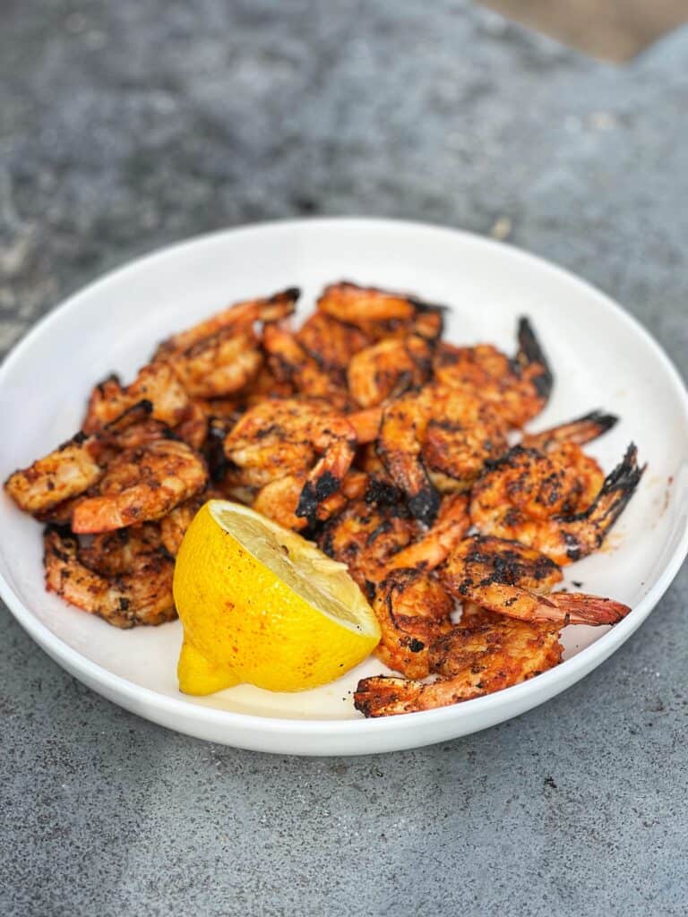 Grilled shrimp in a white bowl with half of a lemon.