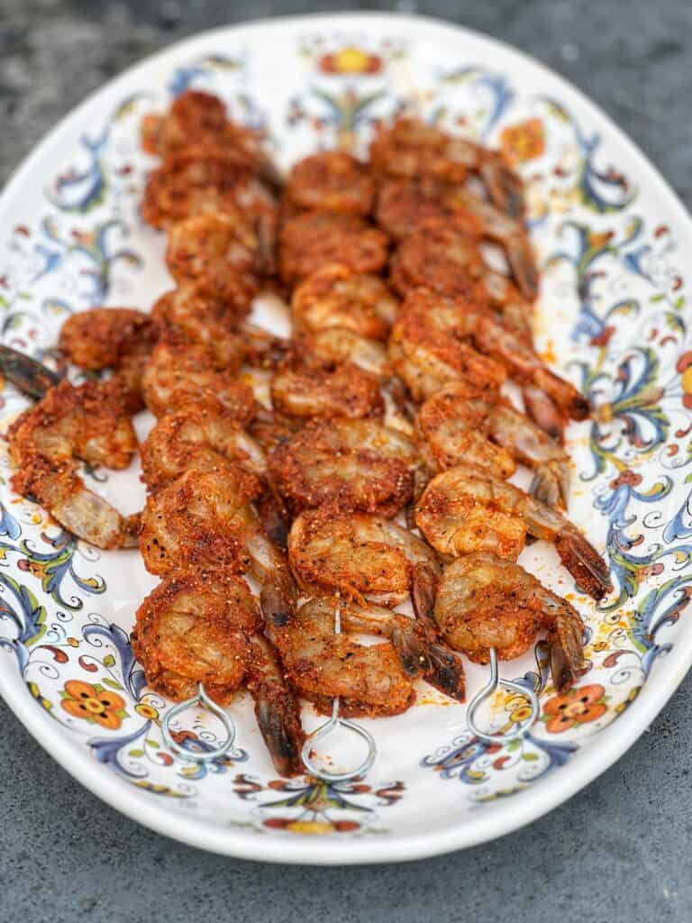 Seasoned shrimp on three metal skewers laying on a ornate platter.