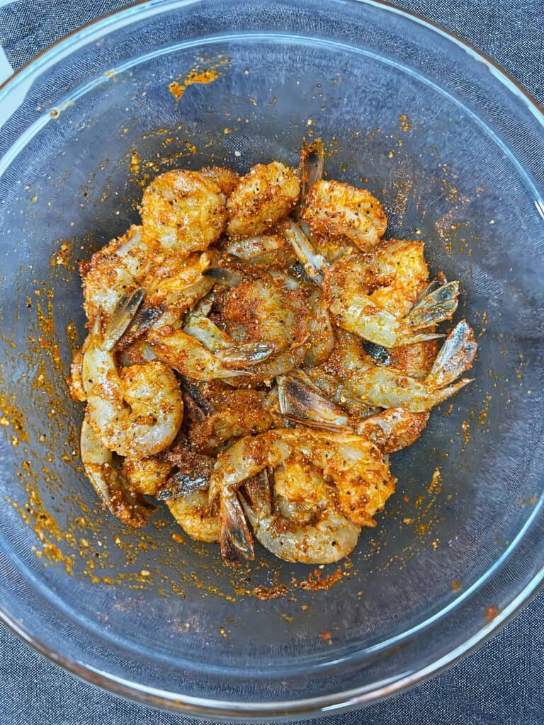 A glass bowl of raw, seasoned tail-on shrimp for a healthy grilled shrimp salad.