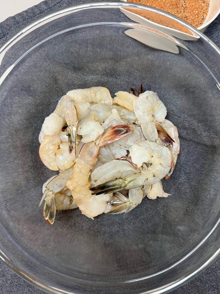 A clear glass bowl filled with tail-on, peeled and deveined shrimp for Healthy Grilled Shrimp Salad.