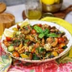 A white bowl filled with cherry tomatoes, cucumber, grilled shrimp and fresh herbs.