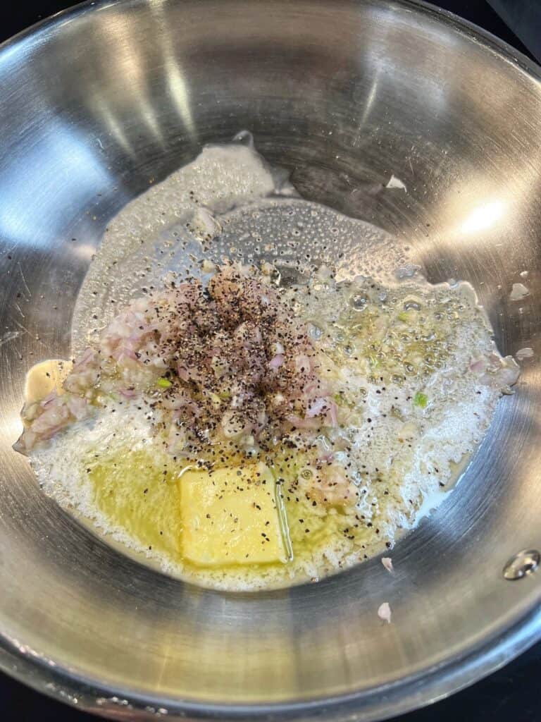 Butter melting in a stainless steel pan with minced shallots, garlic and black pepper.