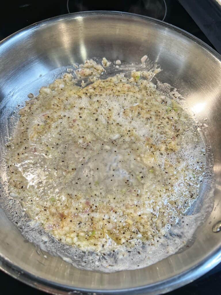 White wine in a butter garlic shallot mixture cooking in a stainless steel pan.