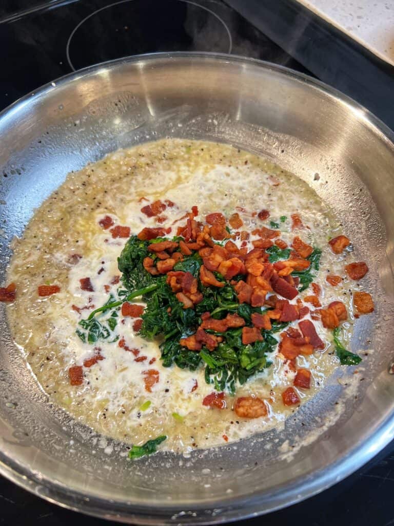 Crisp diced bacon, chopped spinach and heavy cream in a stainless steel pan for the filling for Rockefeller Style Grilled Oysters.