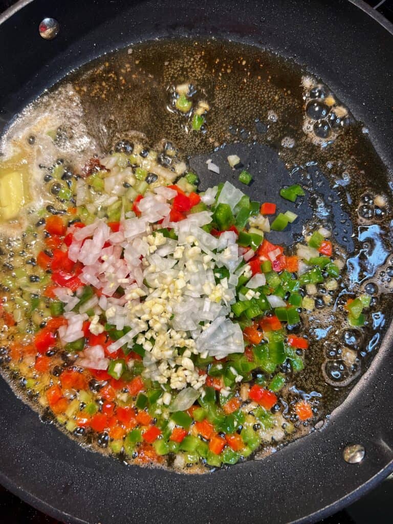 Diced bell peppers, garlic, onions and celery sautéing in a non-stick pan with oil and butter.