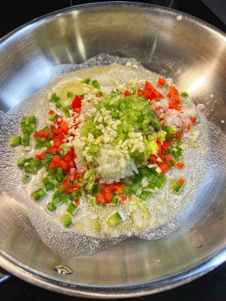 Diced bell peppers, minced celery, minced onion and minced garlic sautéing in a stainless steel pan with olive oil and butter for Creole Crab Baked Oysters.