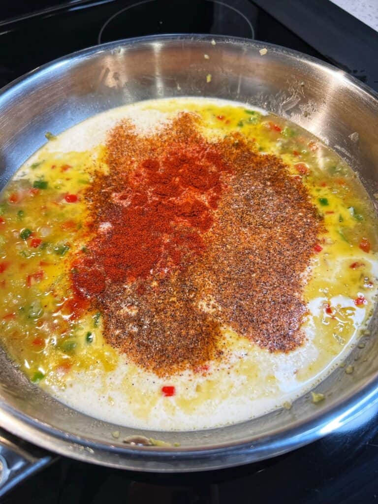 Cream and seasonings added to a pan of sautéed vegetables.