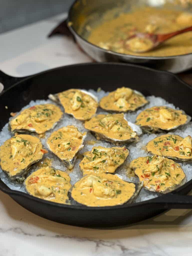 Twelve raw oysters sitting on top of a bed of rock salt in a cast iron pan. The oysters are filled with a Creole crab sauce.