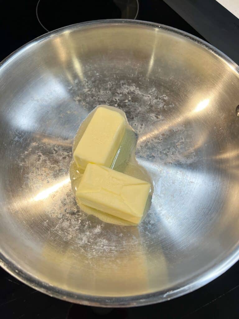 Two half sticks of butter melting in a stainless steel pan.