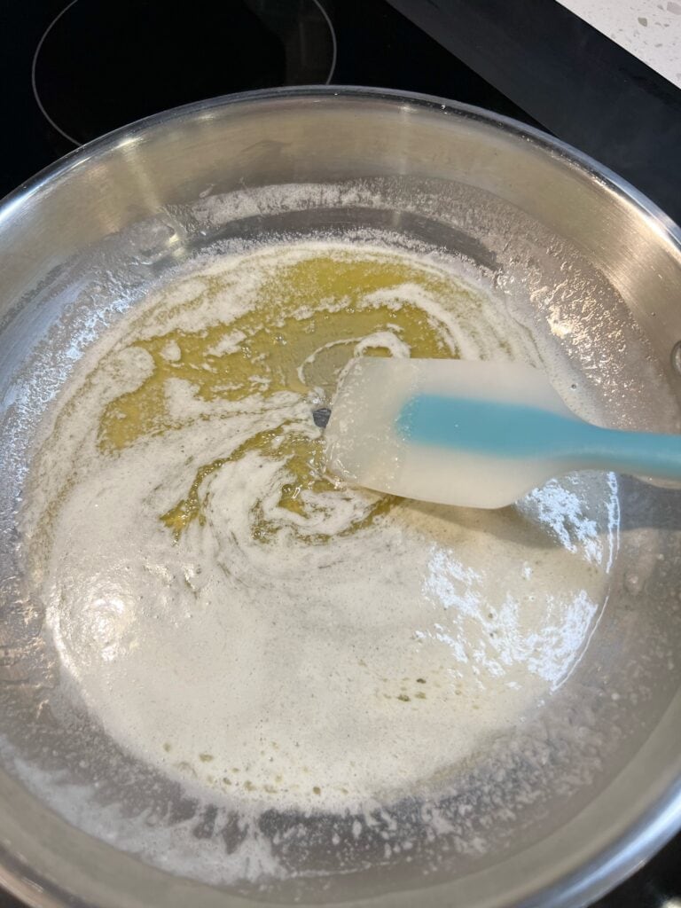 Stirring melted butter in a stainless steel pan with a blue spatula.