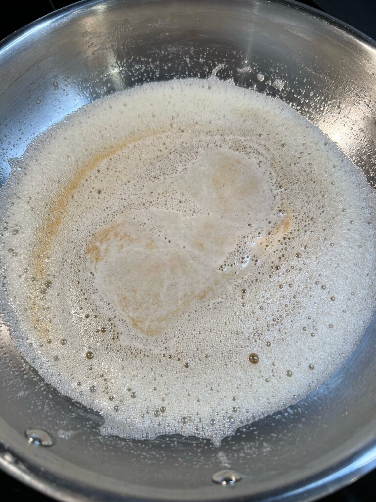 Melted butter foaming and turning a pale brown in a stainless steel pan.