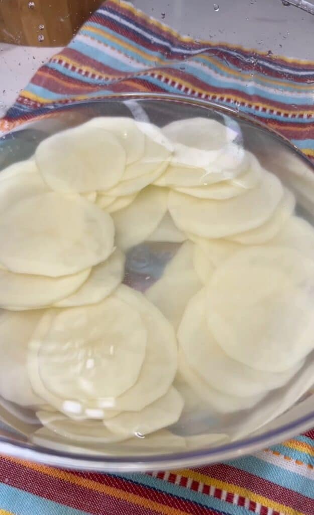 A clear plastic bowl filled with water and thin potato slices.