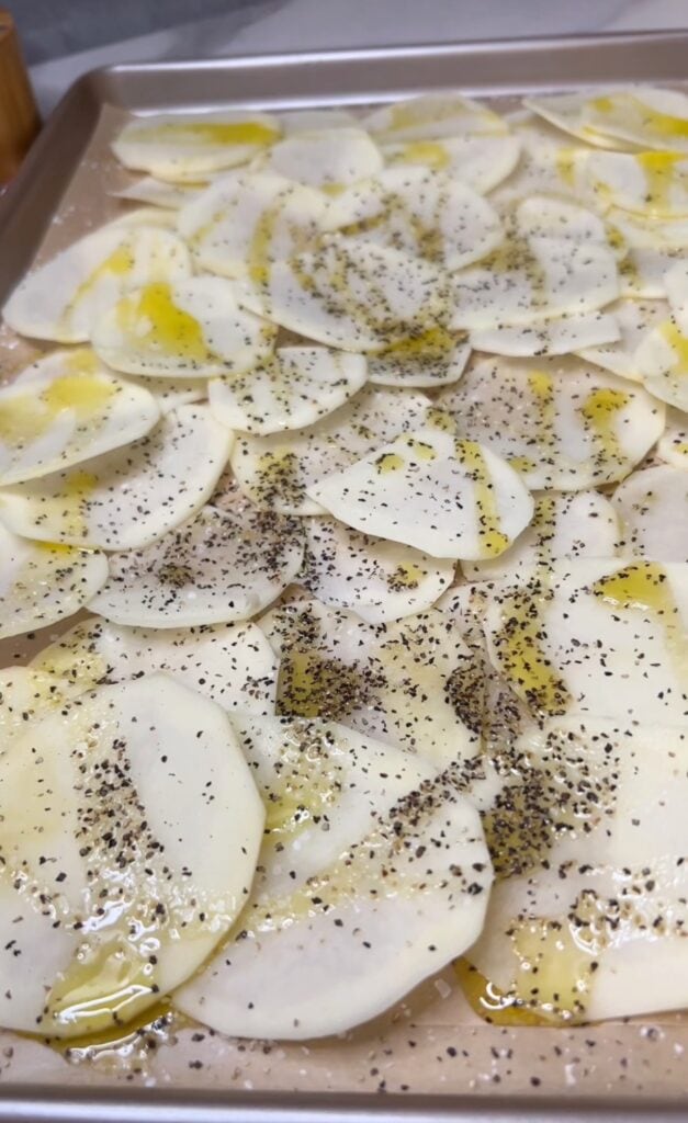 Thinly sliced potatoes seasoned with salt and pepper and coated in olive oil overlapping on a parchment-lined baking sheet.