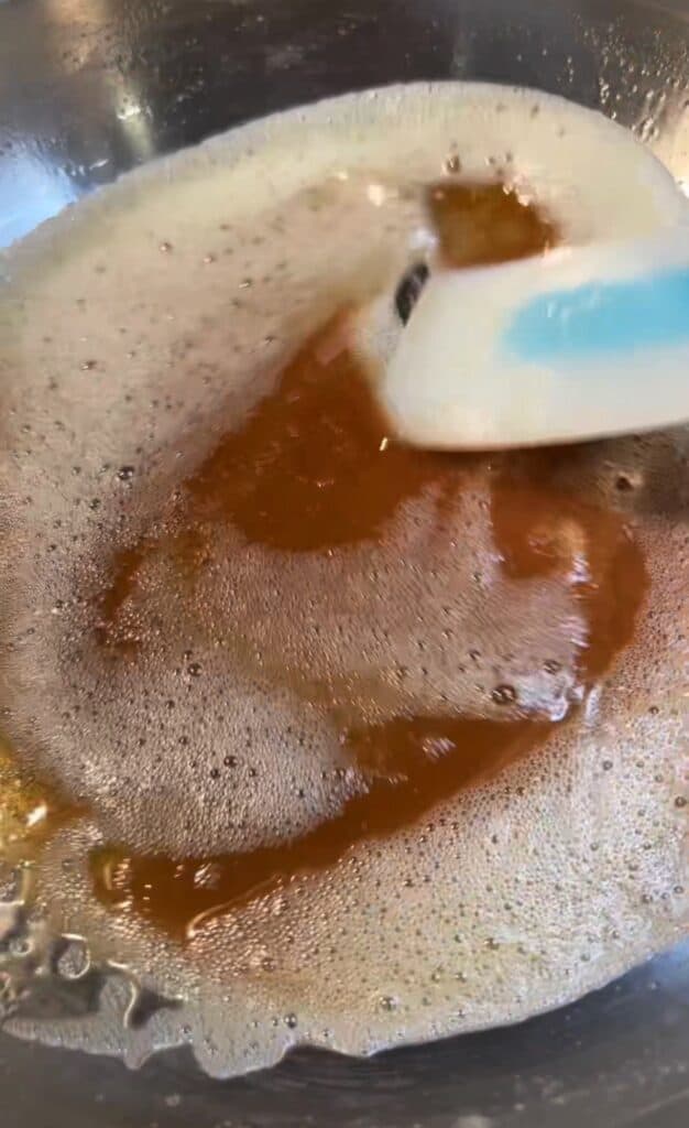 A stainless steel pan of browned butter with a blue spatula stirring the butter.