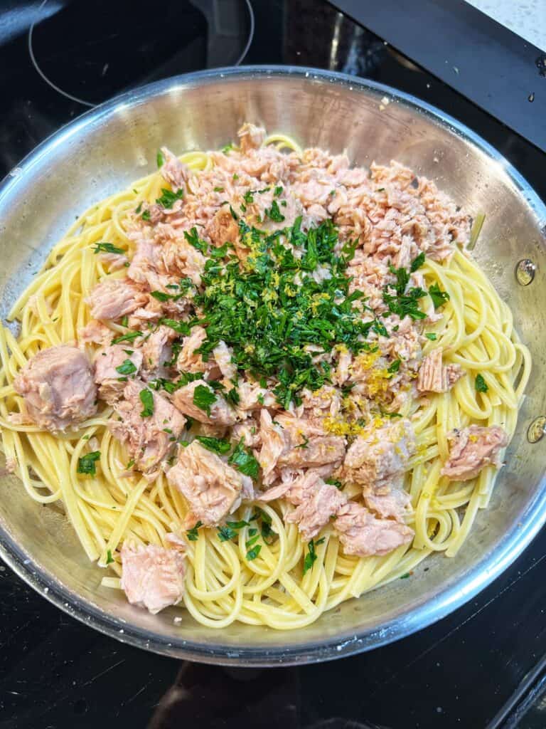 A stainless steel pan of cooked linguine, canned tuna and chopped parsley.