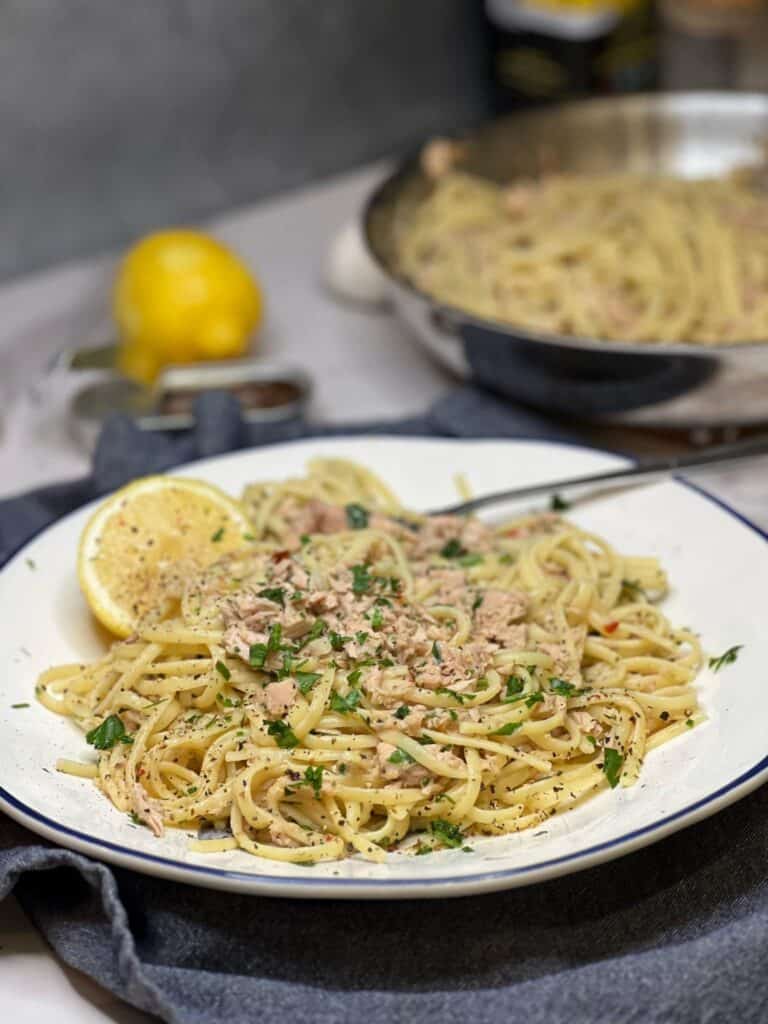 A round plate of canned tuna pasta with lemon. The pasta is garnished with fresh parsley and served with a lemon wedge.