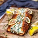 A piece of salmon that has been butterflied and filled with a creamy spinach mixture and seasoned then baked on a parchment lined baking sheet with thinly sliced lemons on top.
