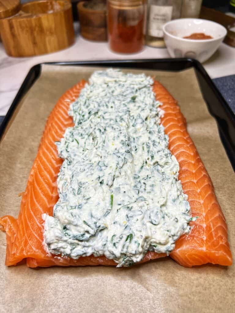A butterflied salmon filet laying on a parchment-lined baking sheet with the middle filled with a creamy spinach mixture.