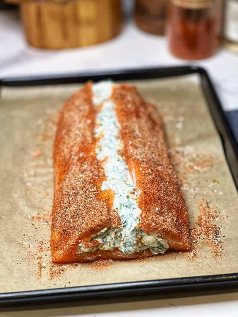 A creamy spinach stuffed salmon filet seasoned and sitting on a parchment-lined baking sheet.