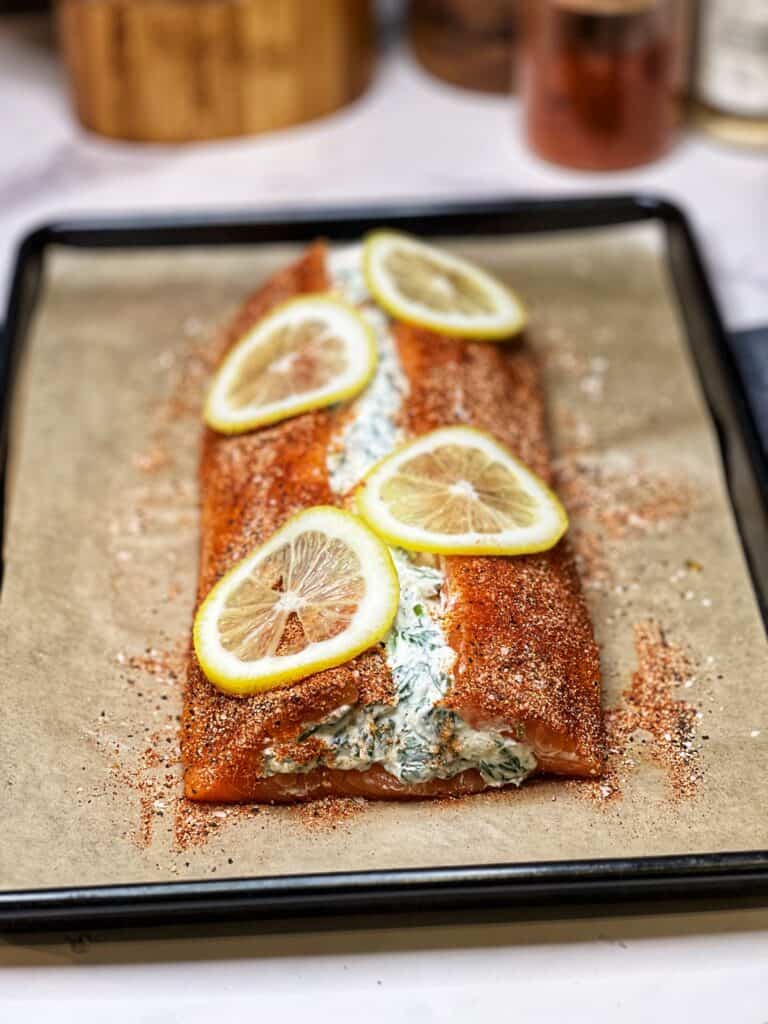 A filet of salmon stuffed with a creamy spinach mixture and seasoned. The filet is also topped with thin lemon slices and is ready to bake.