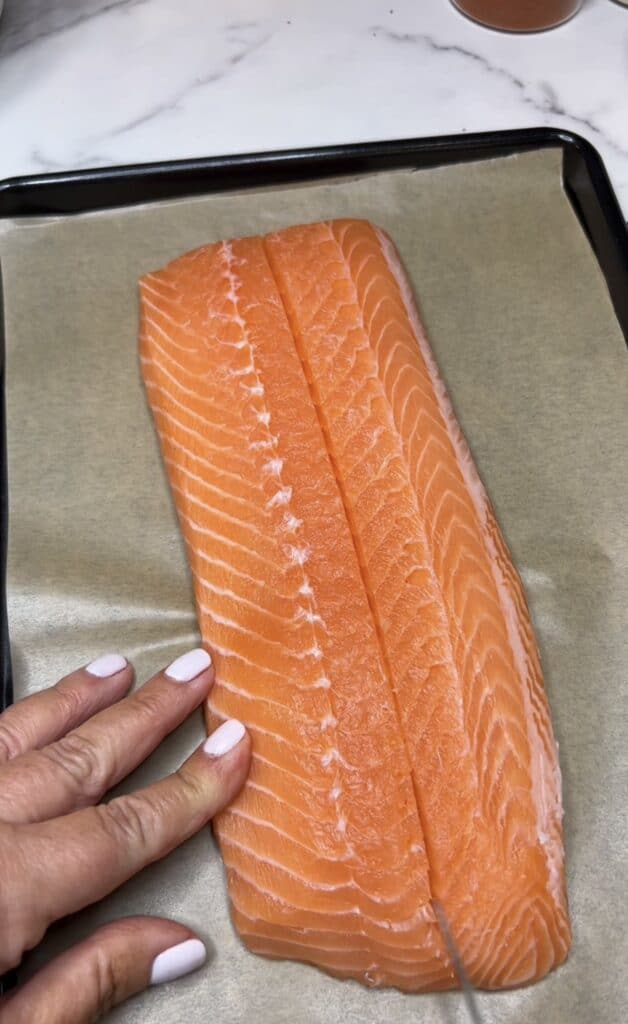 A salmon filet sitting on a piece of parchment with a cut made down the center, but not all the way through.