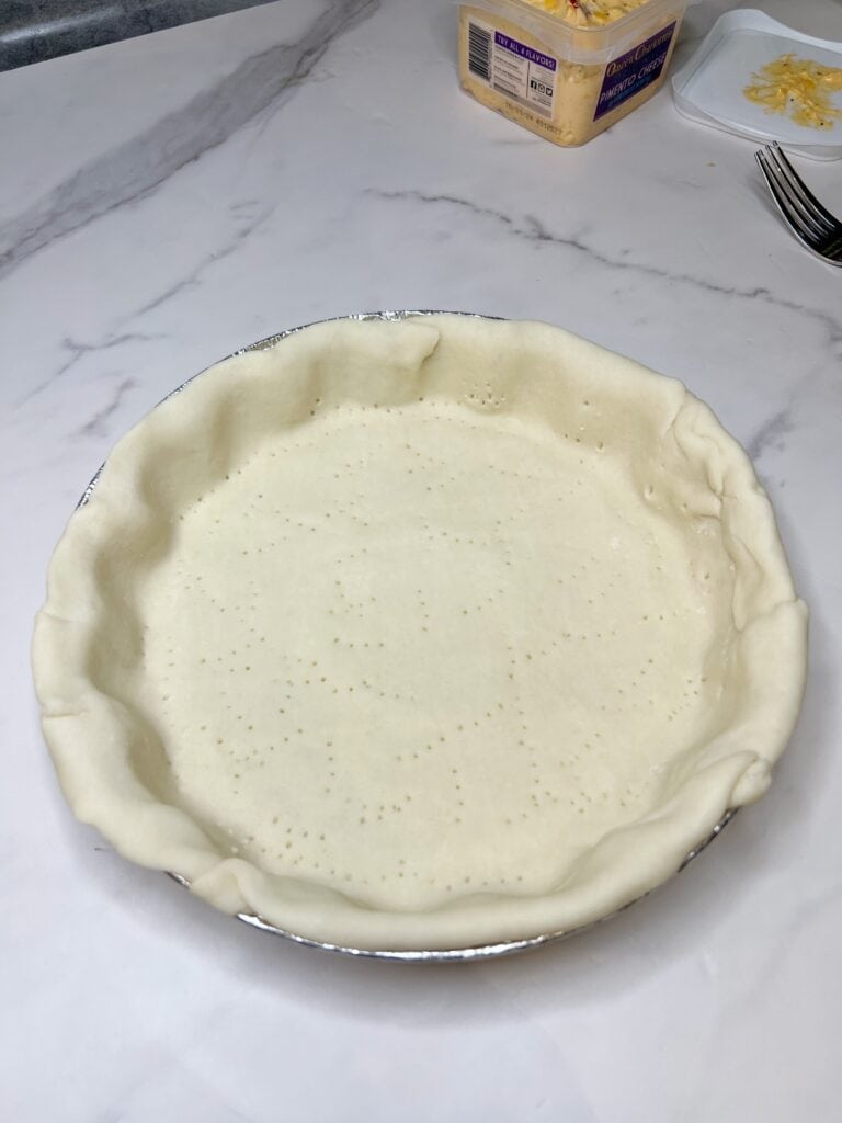 A refrigerated pie crust fit into an aluminum pie tin ready to be baked.