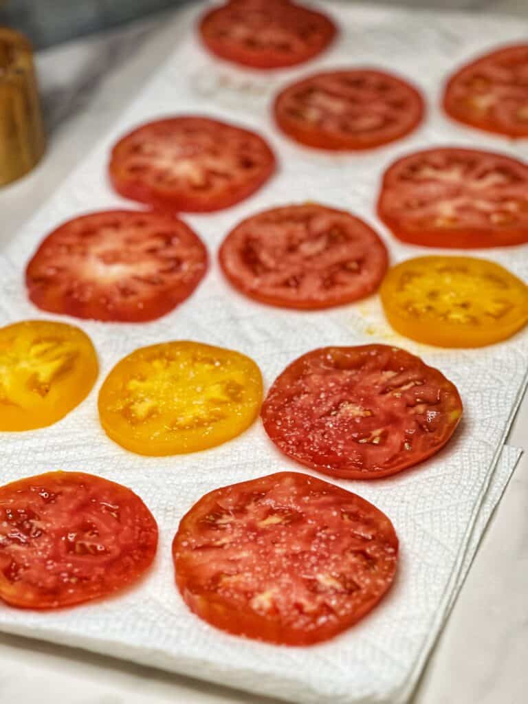Slices of heirloom tomatoes in red and yellow laying on paper towels.