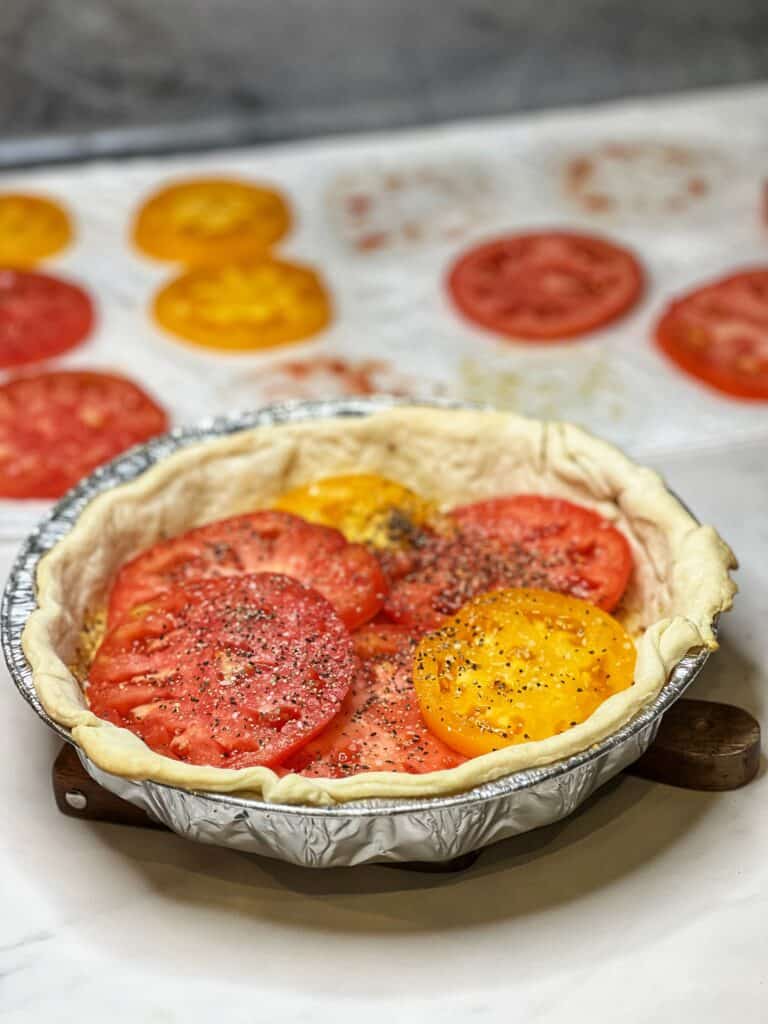 Seasoned tomato slices in a layer in a round pie crust.