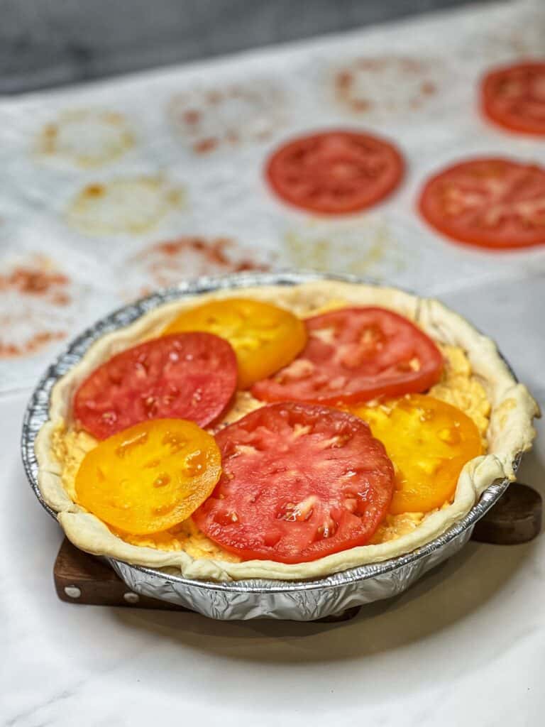Heirloom tomato slices on top of a layer of pimento cheese in a pie dish.