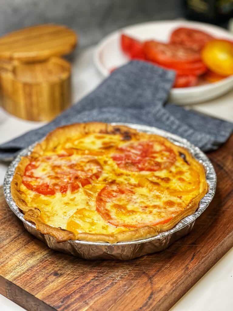 A baked heirloom tomato pie in an aluminum pie tin sitting on a wooden cutting board.