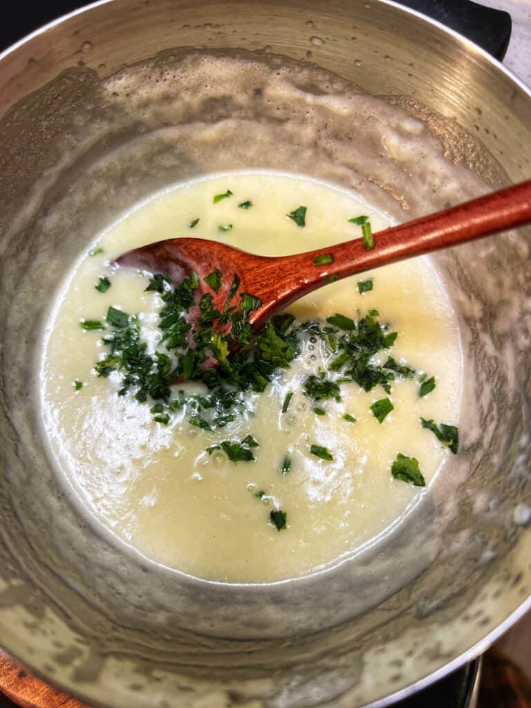 A small stainless steel pot filled with a lemon cream sauce and fresh parsley. A wooden spoon is also in the pot.