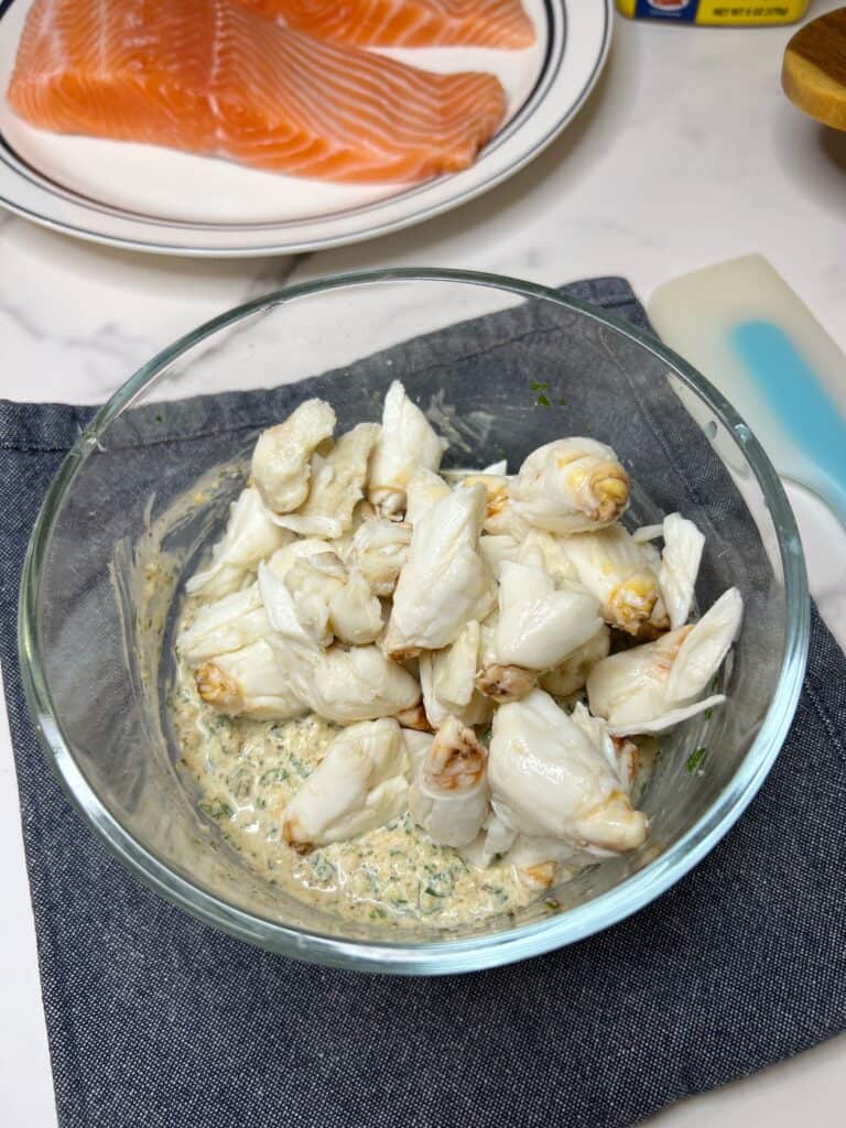Jumbo lump crabmeat in a small glass bowl with a creamy mixture of mayo, mustard, spices and fresh parsley.