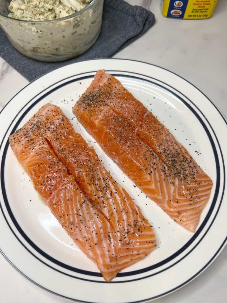 Two seasoned salmon filets that have been slit down the middle sitting on a white plate trimmed in blue.
