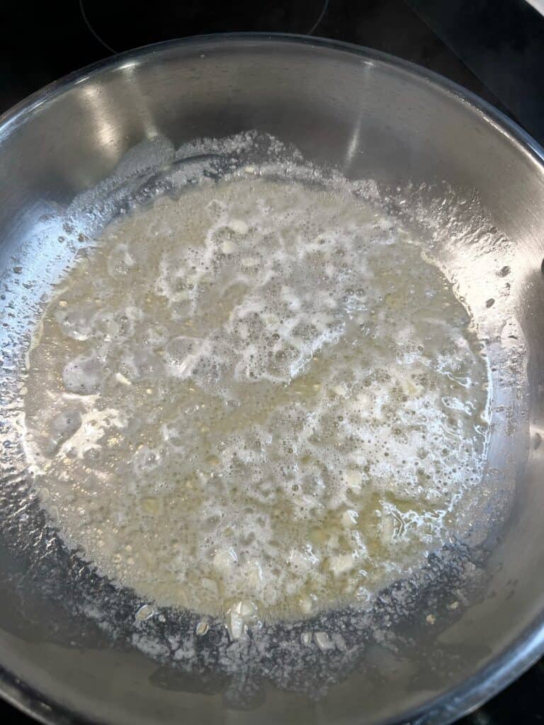 White wine, oil and garlic simmering in a stainless steel pan.