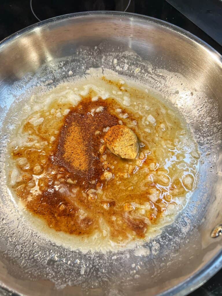 Cajun seasoning and mustard added to a white wine reduction in a stainless steel pan.