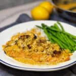 A white deep plate filled with crabmeat stuffed salmon filet covered in a creamy Cajun sauce with asparagus and steamed rice in the back of the plate.