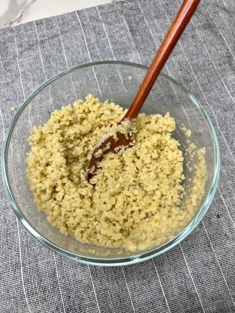 A glass bowl filled with panko breadcrumbs mixed with melted butter. A wooden spoon is in the bowl.