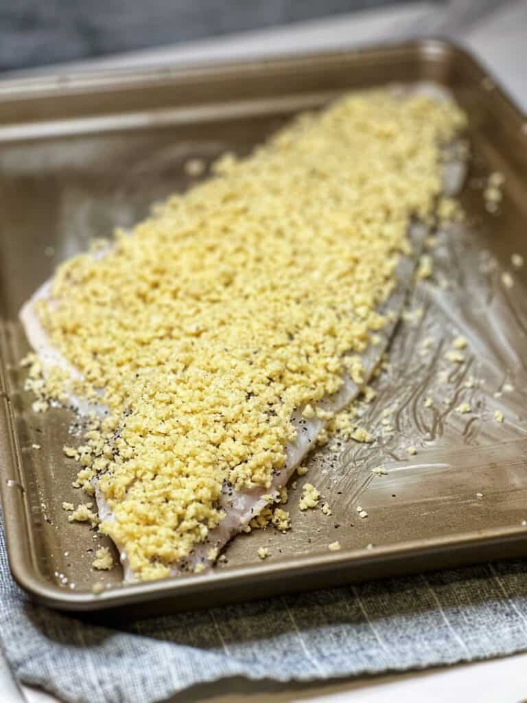 A large piece of haddock sitting on a butter-lined baking sheet topped with panko breadcrumbs mixed with butter.