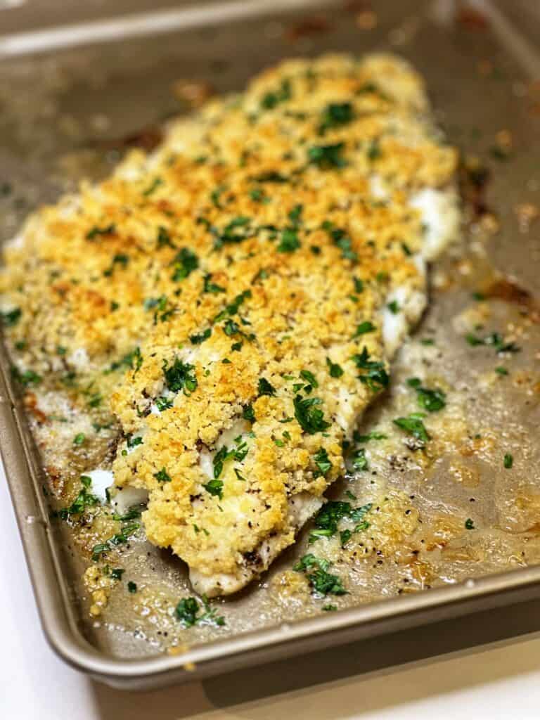 A large piece of panko crusted baked haddock garnished with fresh parsley and sitting on a sheet pan.