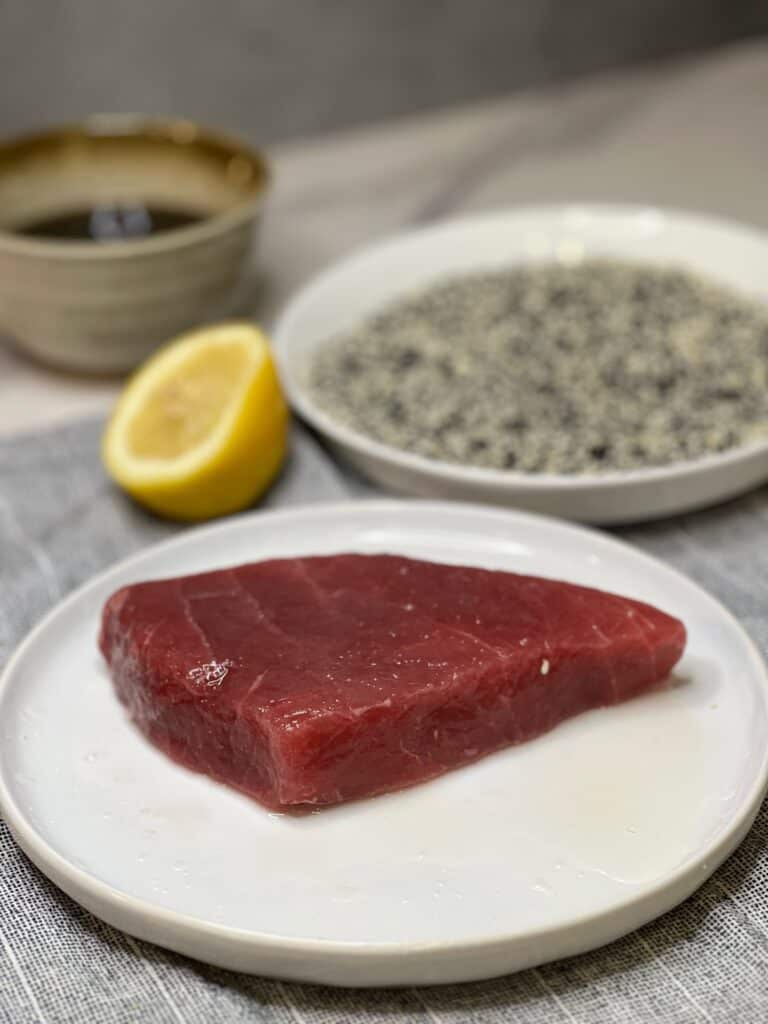A piece of raw, bluefin tuna sitting on a white plate. The tuna has a deep red color.