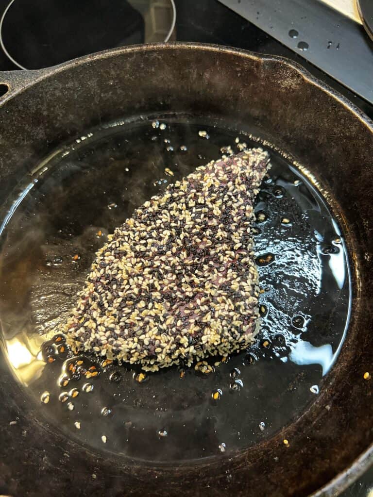 A piece of sesame crusted bluefin tuna starting to sear in a cast iron pan.