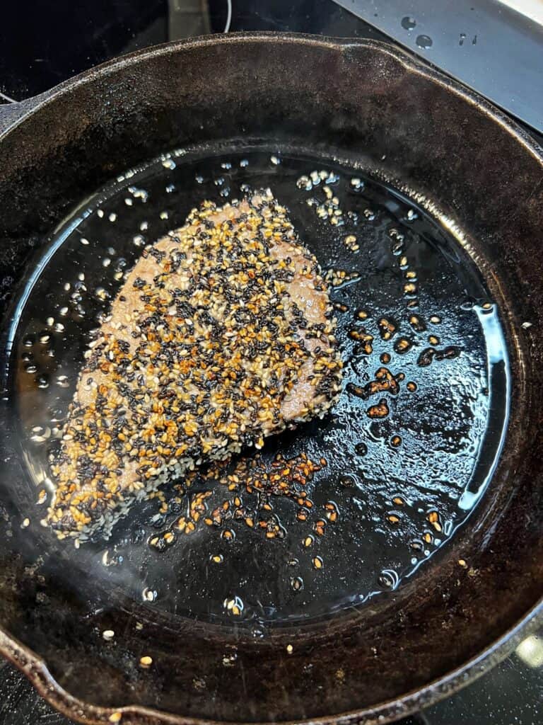A seared piece of sesame crusted bluefin tuna in a cast iron pan.