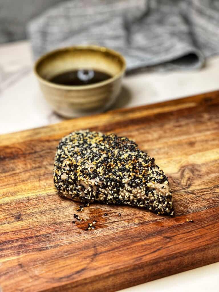A piece of sesame crusted bluefin tuna resting on a wooden cutting board.